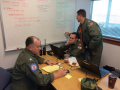 Lt Col Jay Langley, Operations Section Chief discussing details of the sorties with Maj Chris Bailey, Incident Commander as Maj Robert McComas, Mission Staff Assistant updates the task board.